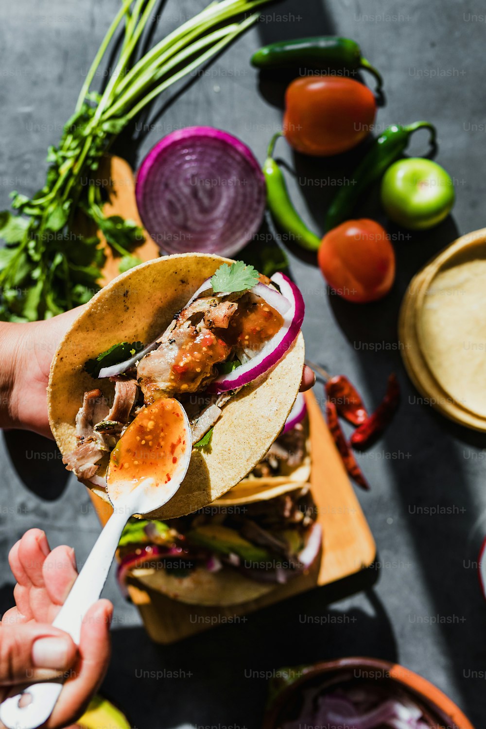 Manos de mujer latina preparando tacos mexicanos con carnitas de cerdo, aguacate, cebolla, cilantro y salsa roja en México