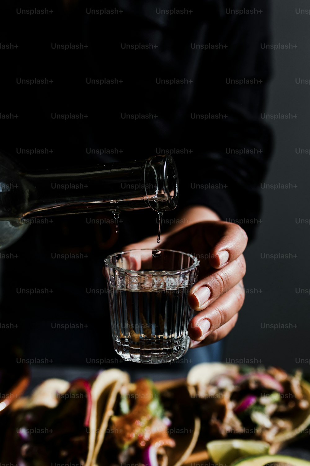 Barman hands serving mexican mezcal shot in a traditional glass with tacos and food at background in Mexico