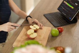 Close-up image, Healthy woman chopping red apples, preparing healthy food while checking stock market chart and graph. Urban lifestyles concept.