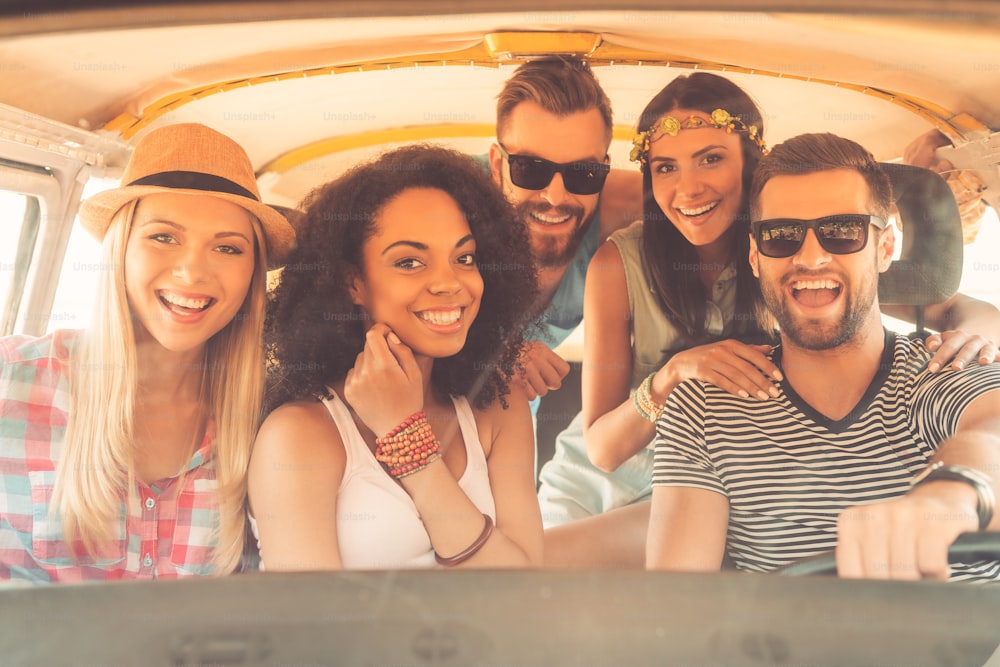 Gruppe fröhlicher junger Leute, die in die Kamera lächeln, während sie zusammen im Minivan sitzen