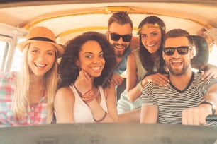 Group of joyful young people smiling at camera while sitting inside of minivan together