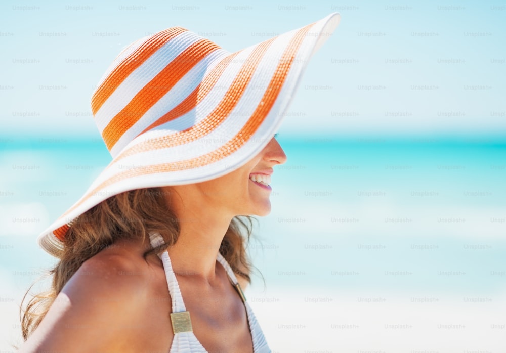 Happy young woman in swimsuit and beach hat looking on copy space