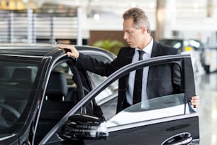 Confident mature man in formalwear opening the car door at the dealership