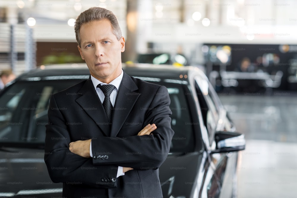 Mature grey hair man in formalwear standing in front of car and looking at camera