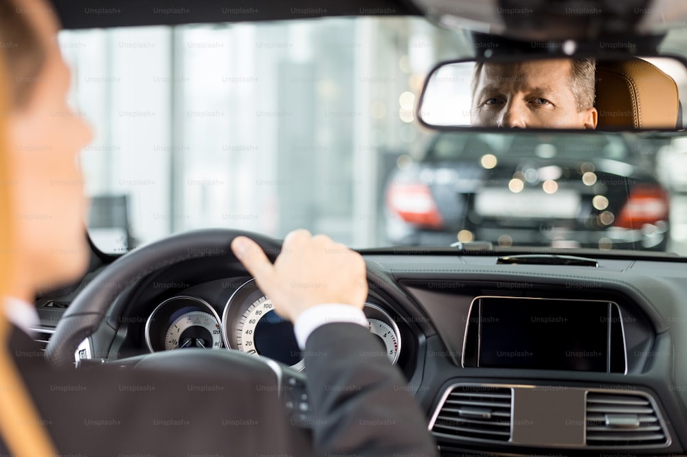 Vista posteriore dell'uomo anziano fiducioso in abbigliamento formale seduto sul posto dei conducenti in auto e guardando lo specchio