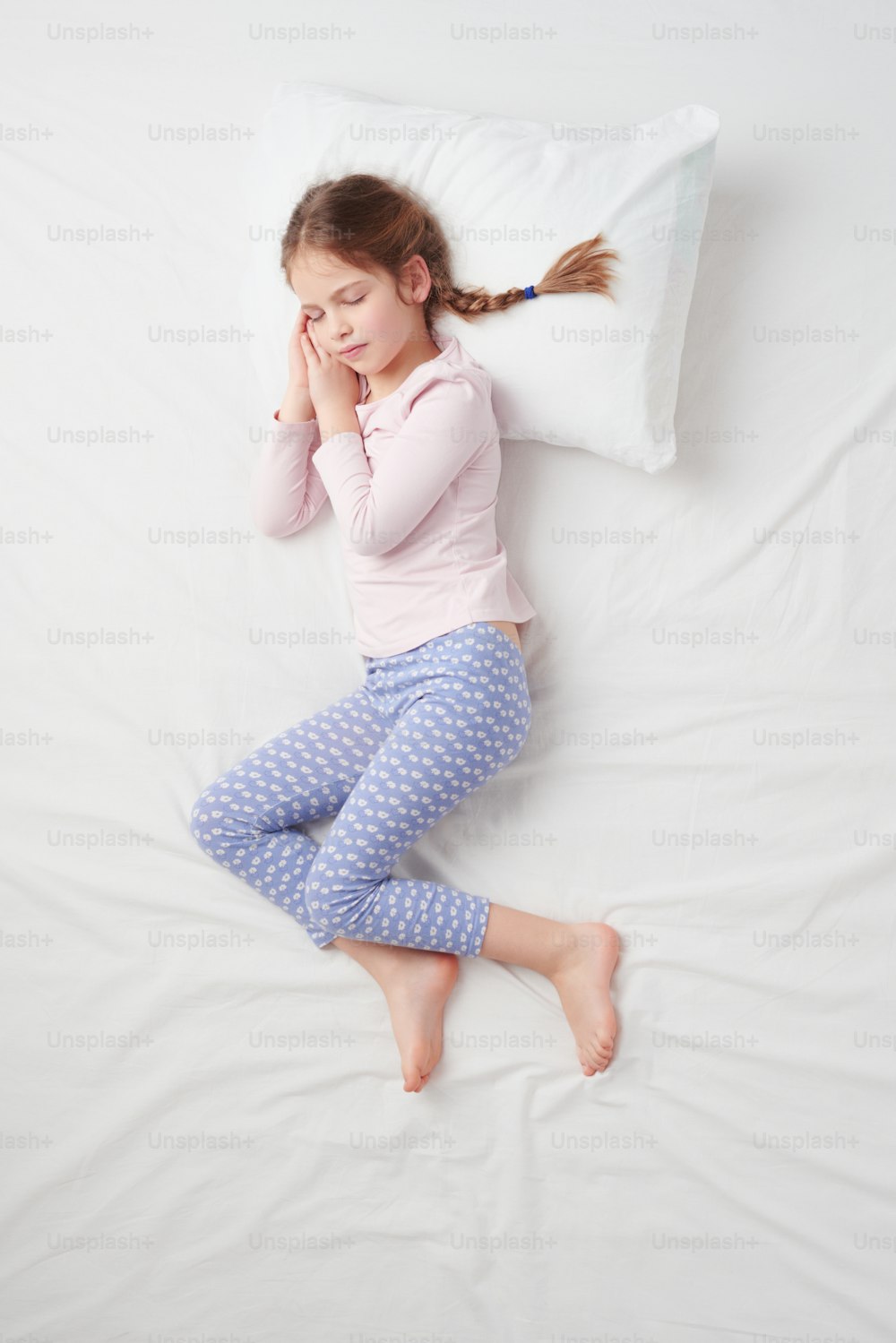Top view photo of little cute girl with pigtails sleeping on white bed. Concept of sleeping poses