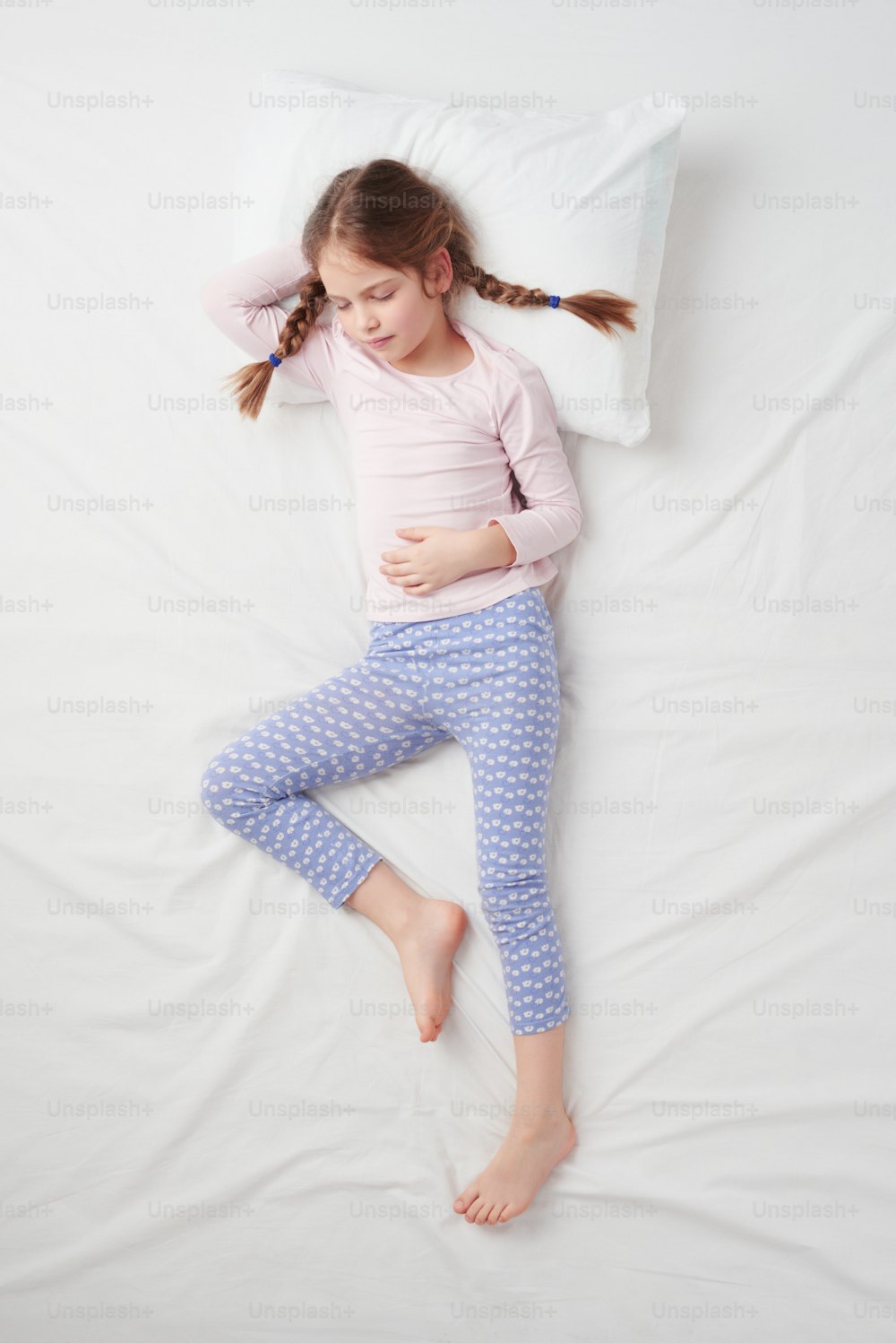 Top view photo of little cute girl with pigtails sleeping on white bed. Concept of sleeping poses