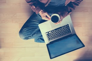 Ein Mann, der mit einem Laptop arbeitet und eine Tasse Kaffee in der Hand hält.