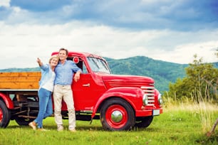 Senior couple standing by their vintage red car