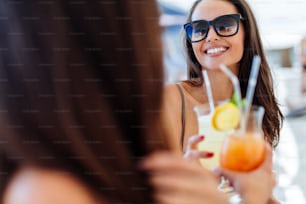 Amigas alegres bebiendo cócteles en verano y sonriendo