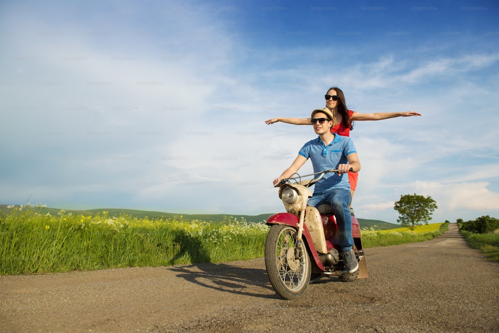 Happy young couple in love on retro motorbike driving togetger and ejoying the trip in green field