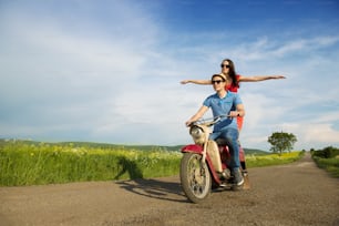 Happy young couple in love on retro motorbike driving togetger and ejoying the trip in green field