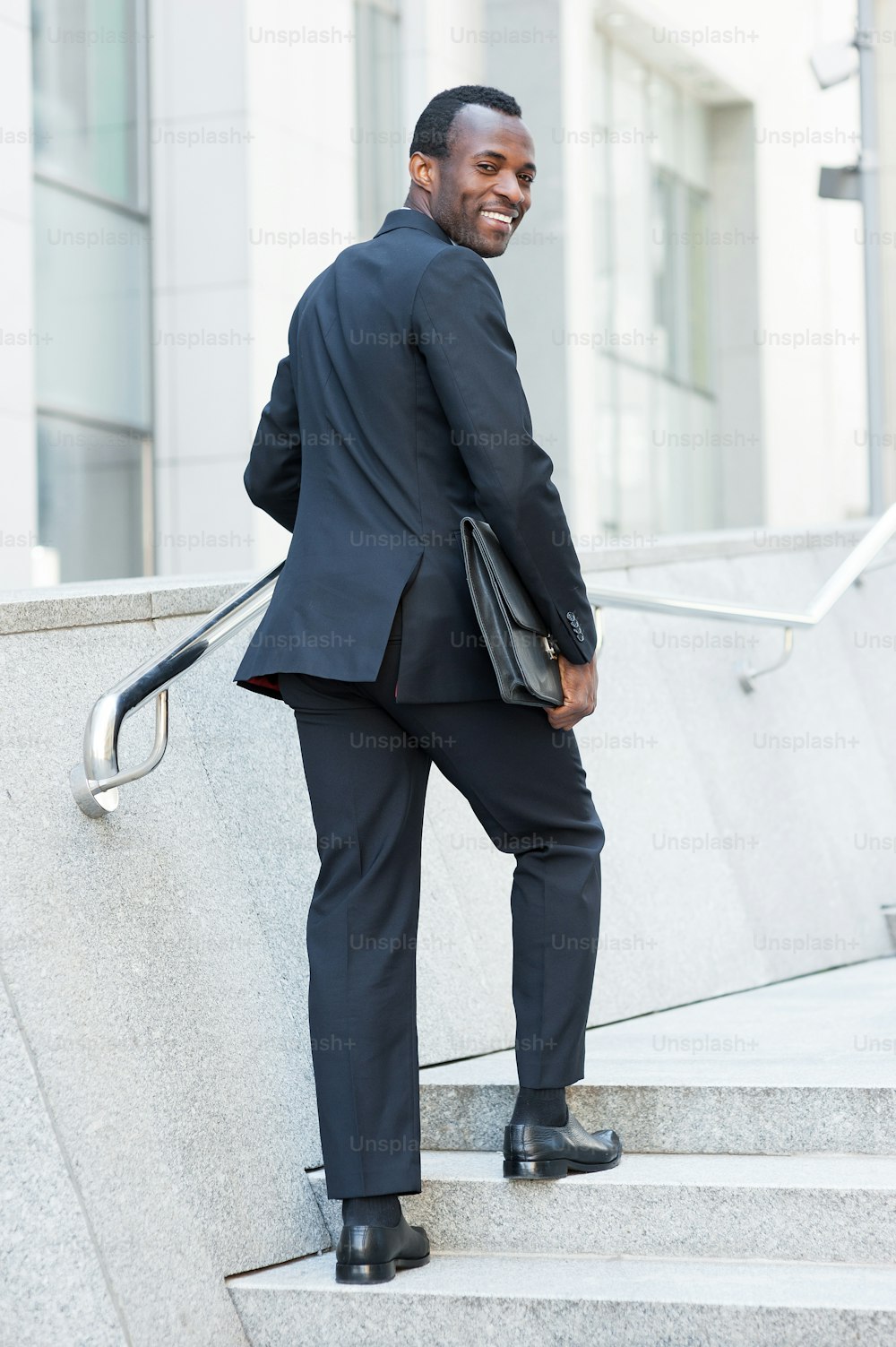 Jovem africano alegre em traje formal subindo pela escada e olhando por cima do ombro