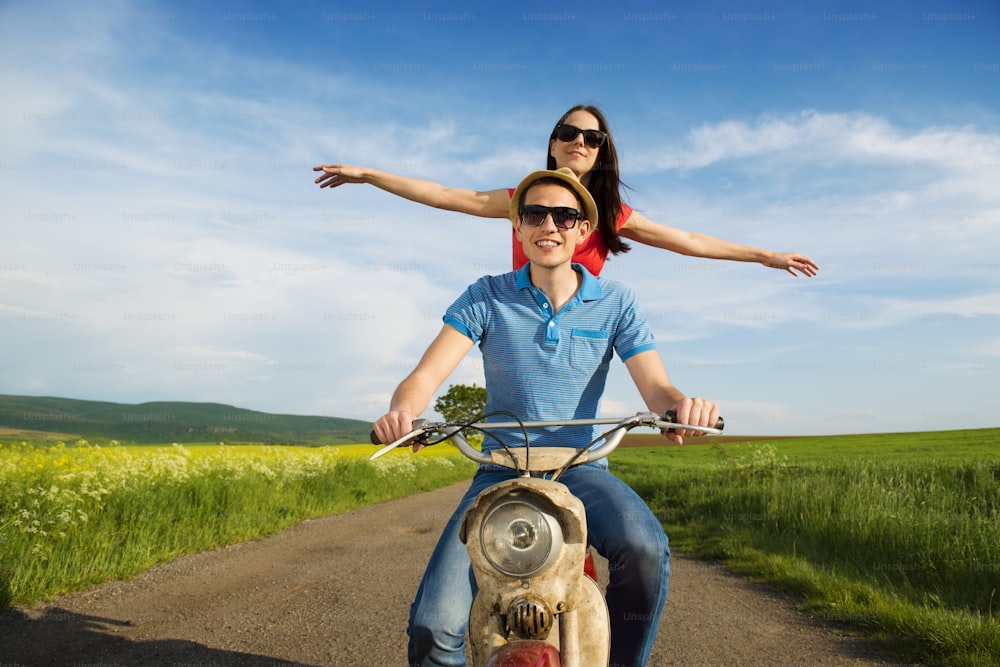 Happy young couple in love on retro motorbike driving togetger and ejoying the trip in green field