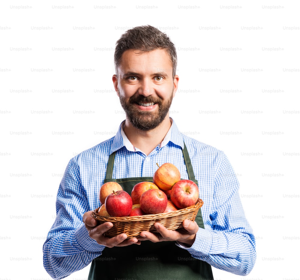 Young handsome gardener holding a basket full of apples. Studio shot on white background