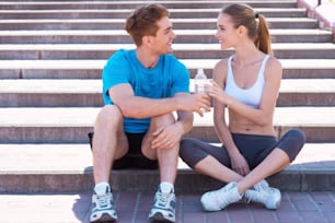 Side view of beautiful young couple in sports clothing sitting on stairs face to face and smiling