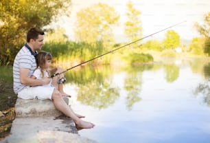 Pai jovem feliz pescando no lago com sua filhinha