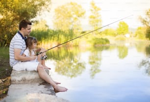 Happy young father fishing on the lake with his little daughter