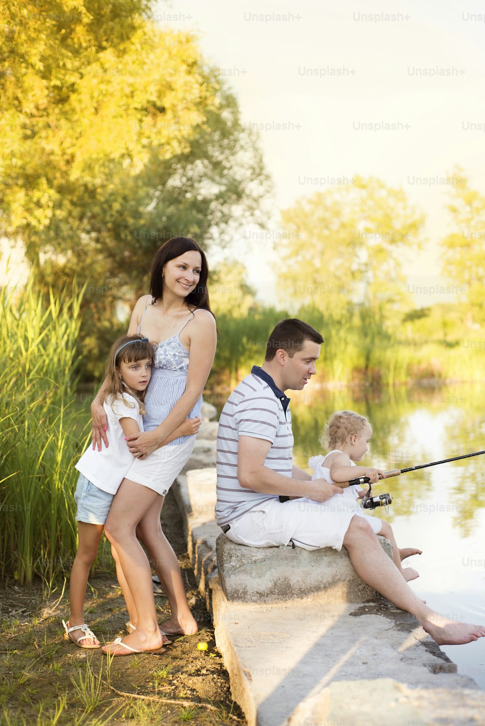 夏��に池で釣りをする子供と若い幸せな家族