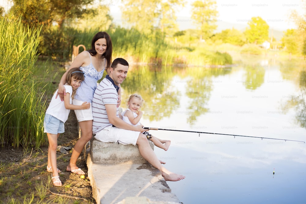 Young happy family with kids fishing in pond in summer