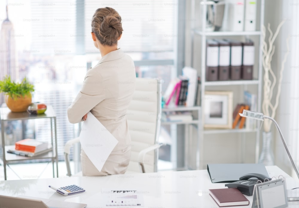 Business woman standing with document in office. rear view