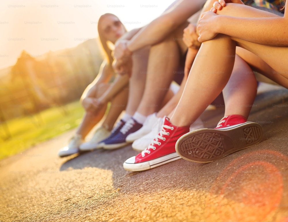 Legs and sneakers of teenage boys and girls sitting on the sidewalk