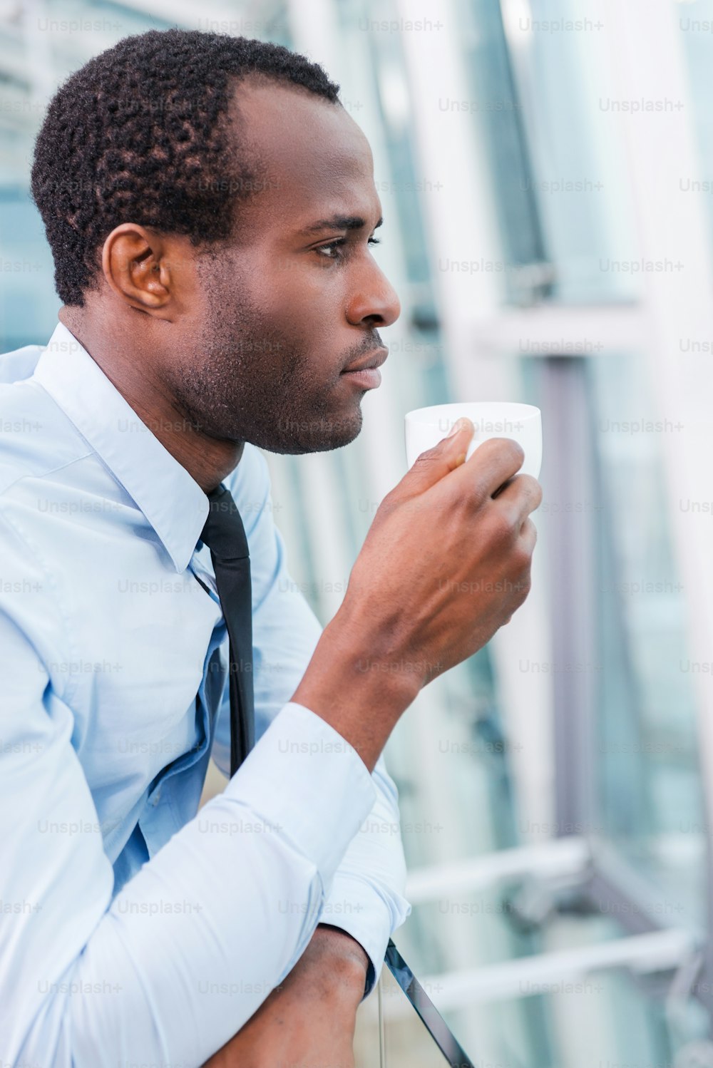 Side view of thoughtful young African man in shirt and tie holding coffee cup and looking away