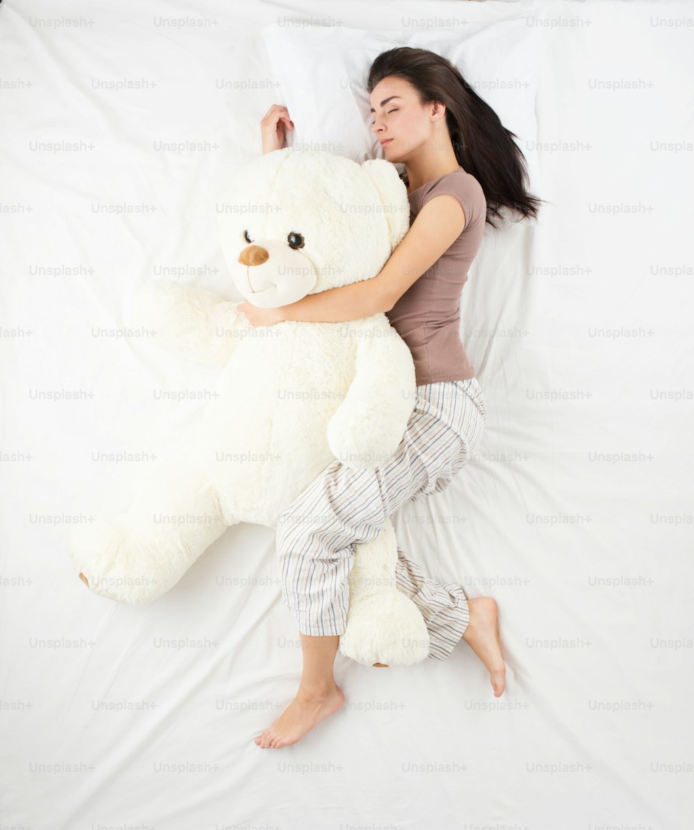 Young woman sleeping in an embrace with a large white teddy bear. Top view photo. Woman with brown hair