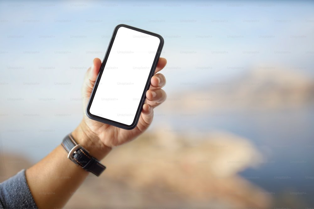Primer plano de un hombre no identificable que muestra una pantalla en blanco, un teléfono inteligente y un fondo borroso del parque natural.