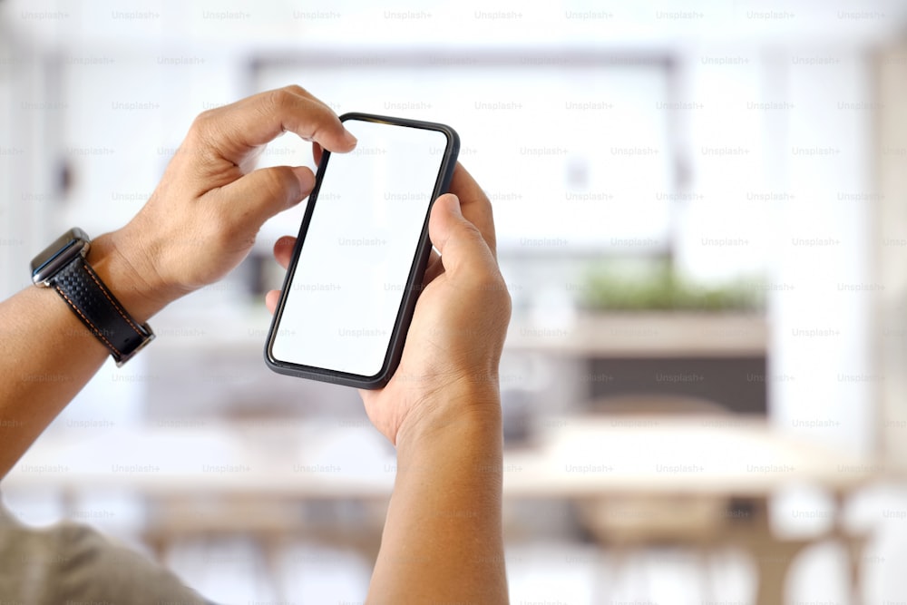 Mockup image of man hands holding black mobile phone with blank white screen in office