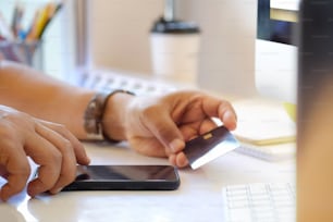 Online-Zahlungskonzept. Mann mit Kreditkarte mit Handy und Kaffeetasse auf weißem Schreibtisch.