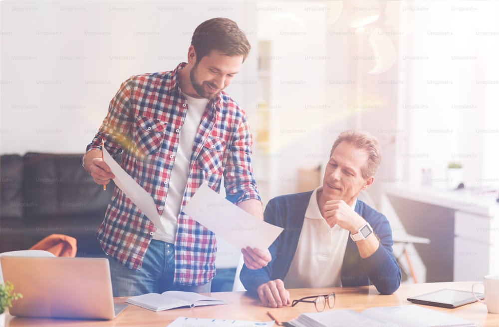 Trabajar en cooperación. Colegas experimentados sonrientes positivos sentados en la oficina y discutiendo proyectos mientras trabajan juntos