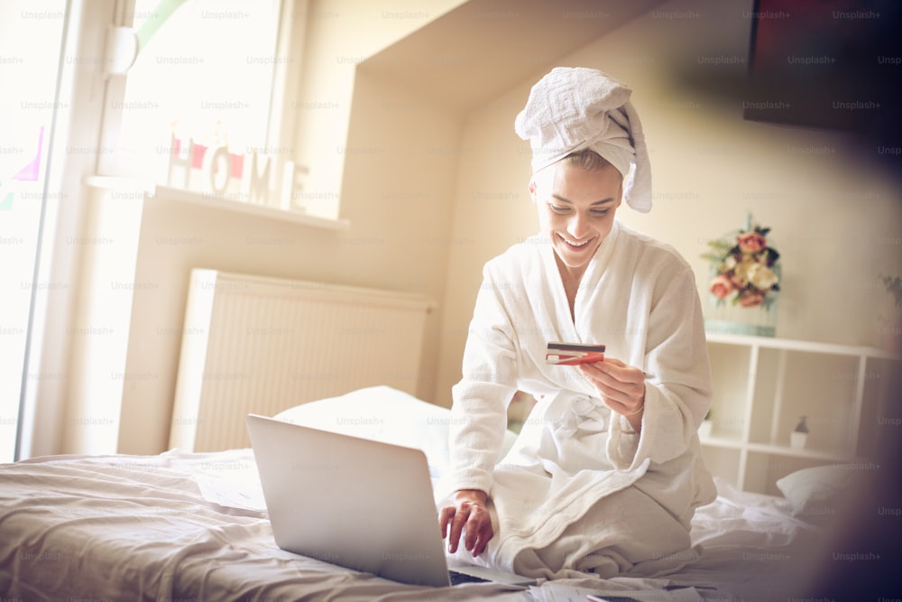 Smiling woman checking credit card on laptop.