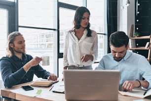 Jovens colegas modernos em roupas casuais inteligentes trabalhando juntos enquanto passam o tempo no escritório criativo