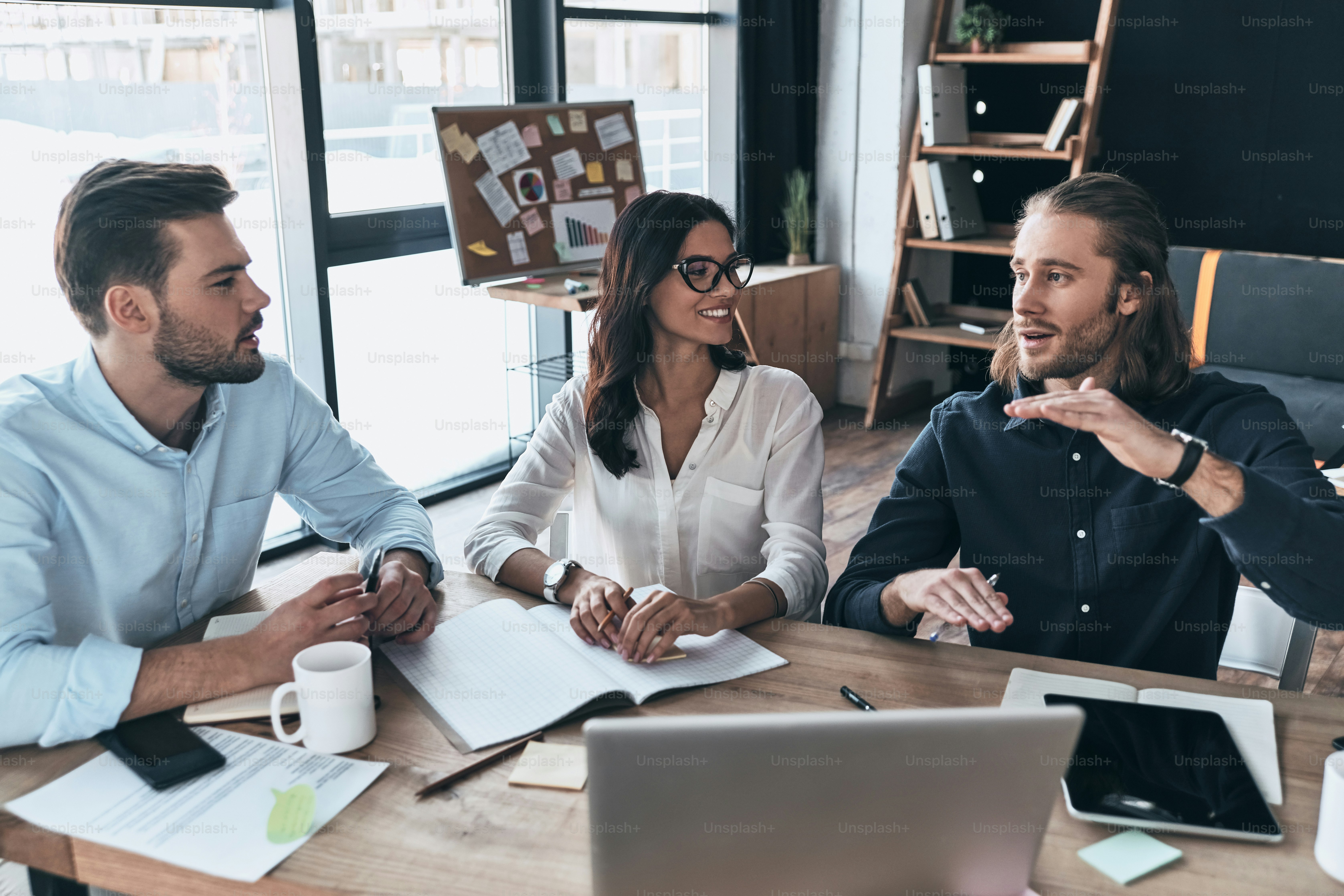 Top view of young modern people in smart casual wear working together and smiling while sitting in the creative office