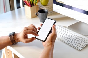 Abgeschnittene Aufnahme eines Mannes, der ein Handy mit leerem Bildschirm auf dem Schreibtisch hält. Bildschirm-Smartphone für grafische Display-Montage.