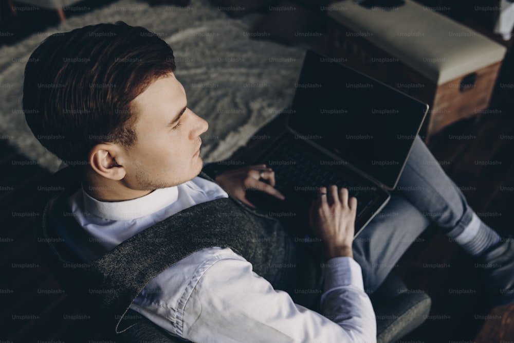Vista de Uper de un hermoso joven hombre de negocios sentado en la oficina en un char y trabajando en la computadora portátil mientras mira hacia otro lado.