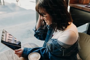 Upper view of a cute young woman sitting in a coffee shop and using a tablet smiling and playing with her hair.