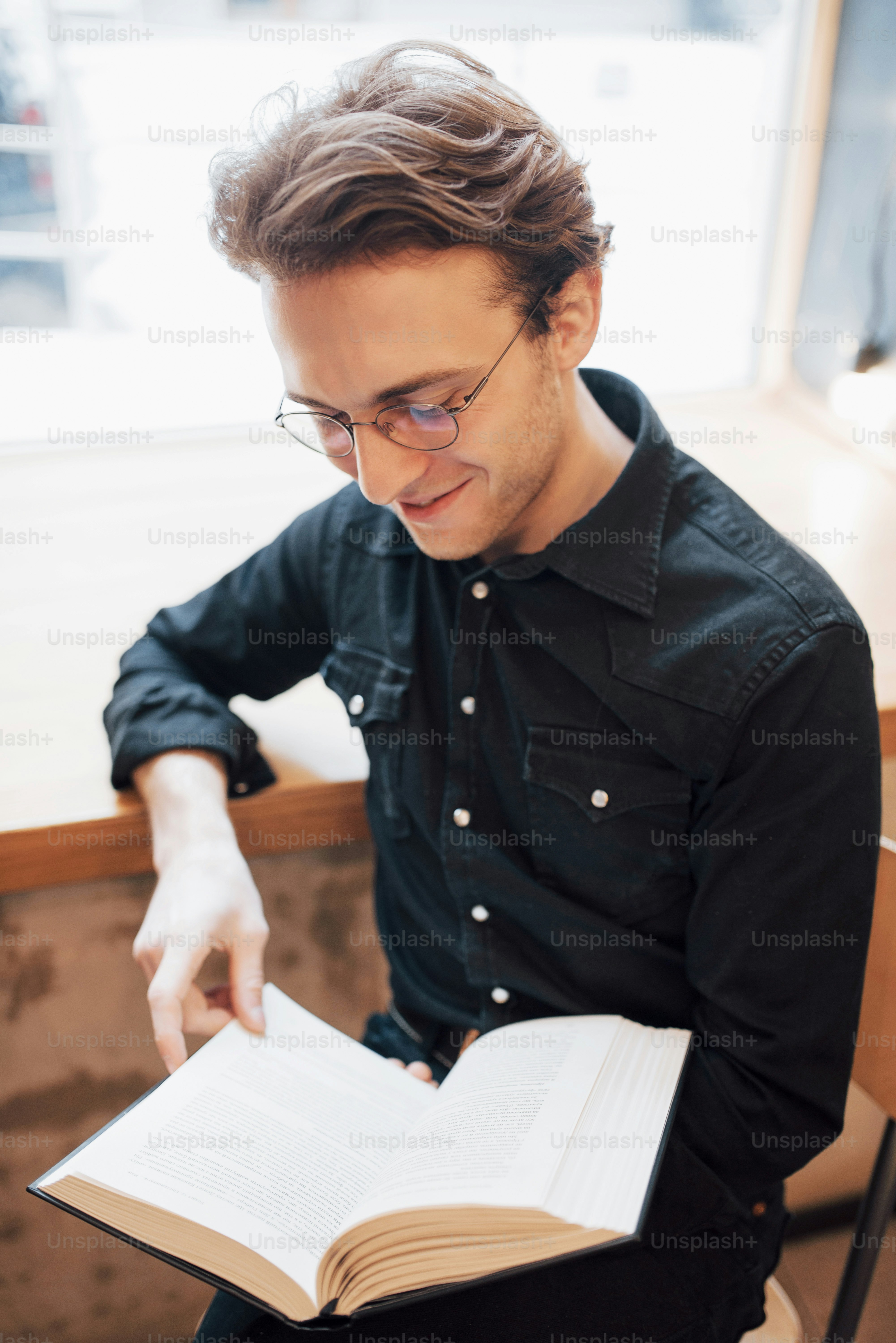 Cheerful businessman dressed in white shirt sitting in cafe and reading a book.