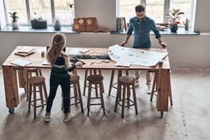 Top view of young colleagues in smart casual wear using blueprint while working in the creative working space