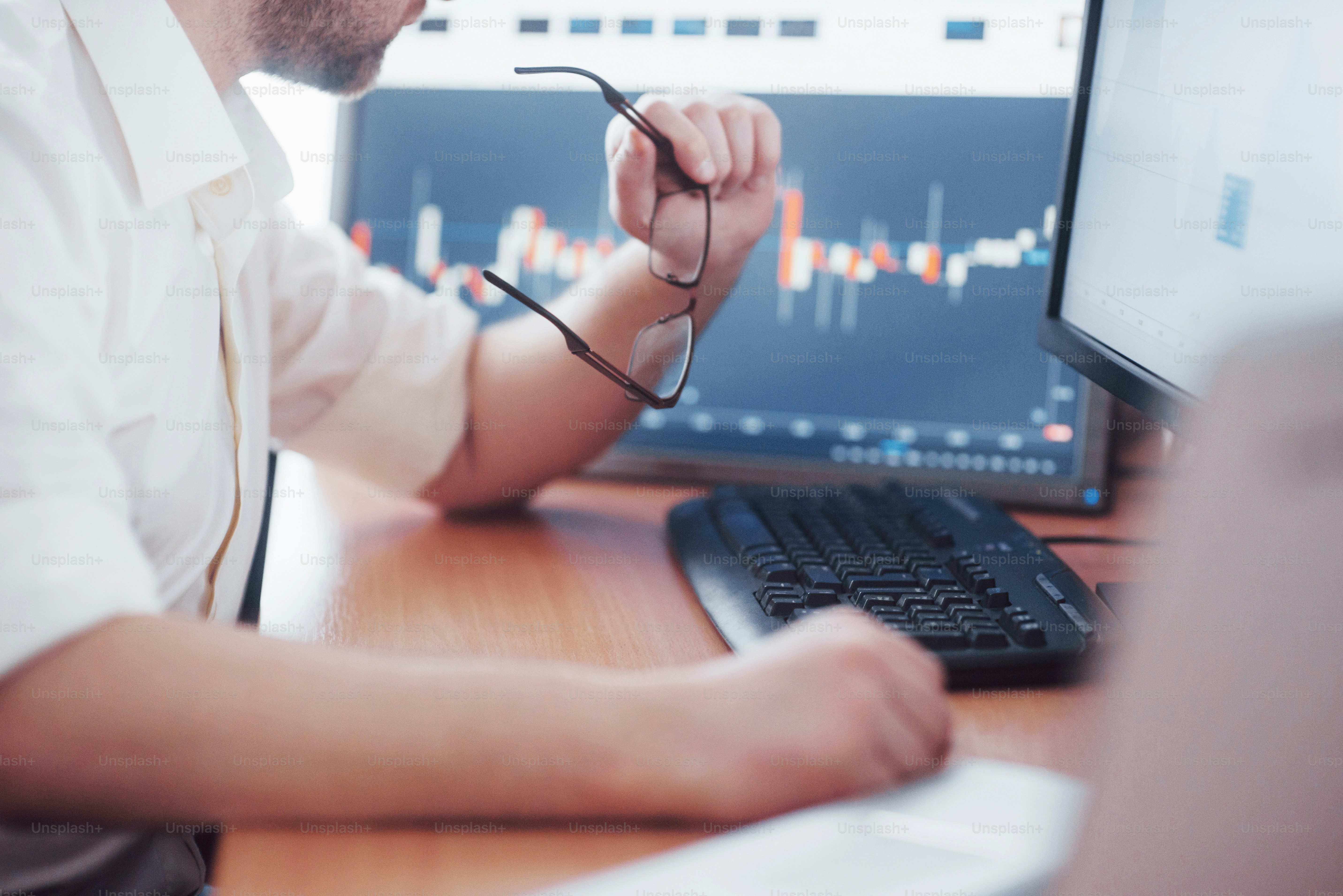 Analyzing data. Close up of a young businessman who holds glasses and looks at the gff while working in a creative office.