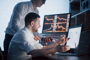 Team of stockbrokers are having a conversation in a dark office with display screens. Analyzing data, graphs and reports for investment purposes. Creative teamwork traders.