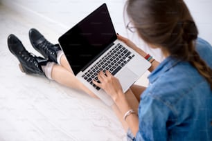 Retrato en primer plano de las manos de la mujer trabajando en el teclado de su computadora portátil, mientras está sentada en una flor blanca sosteniendo la computadora en sus largas piernas.