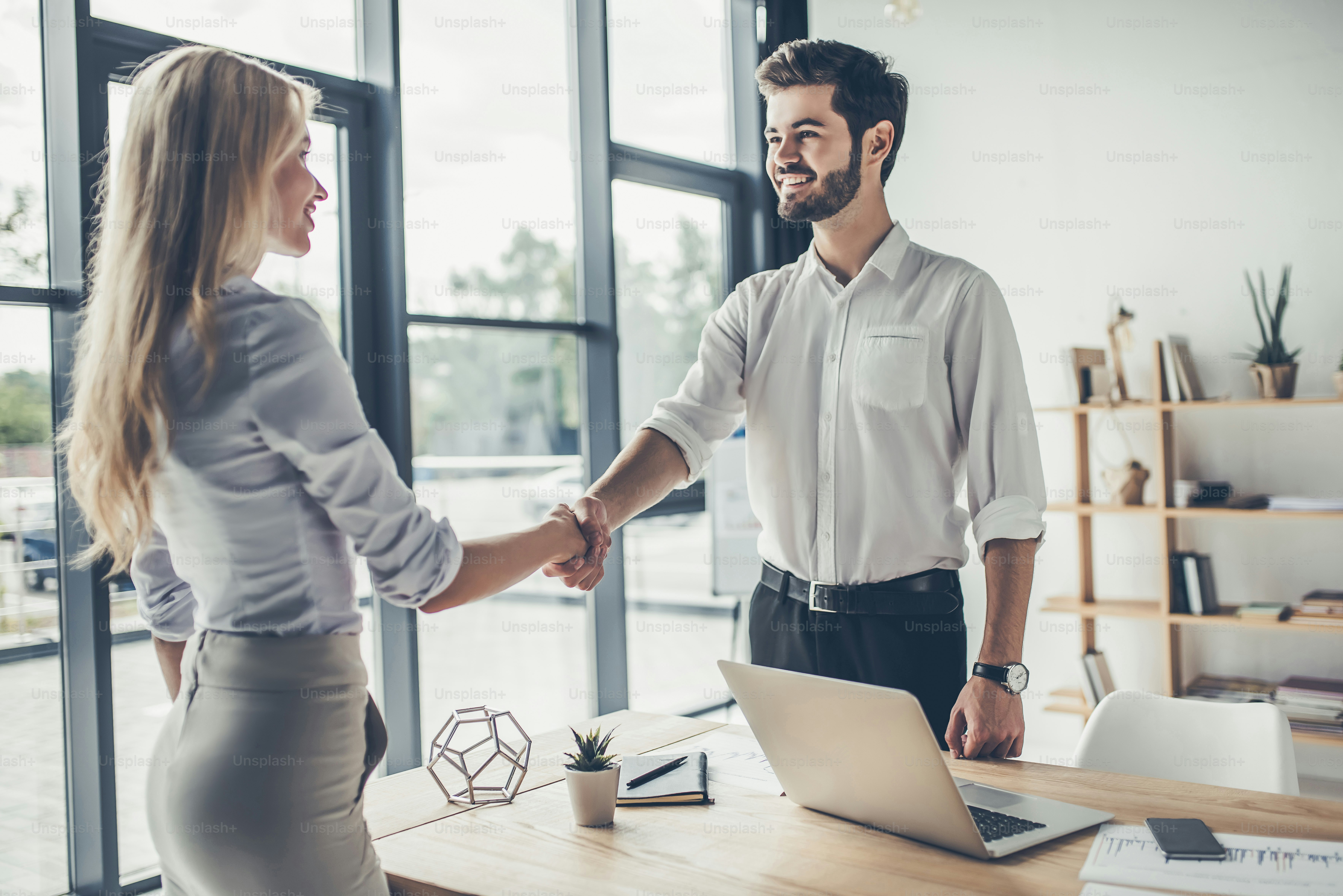 Attractive young businessman and businesswoman are working in modern light office. Shaking hands.