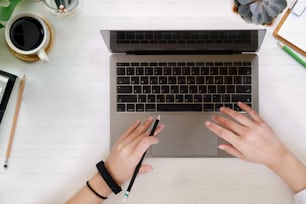 Espacio de trabajo de la vista superior manos femeninas escribiendo computadora portátil en el escritorio. Escritorio de oficina en casa plano.