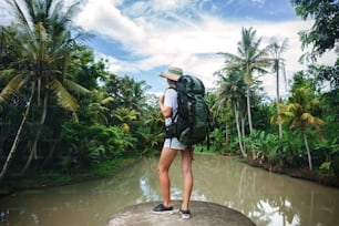 Brave traveling woman with backpack standing on the edge near big tropical river