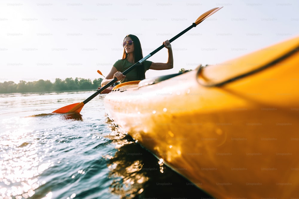 Vista angolare bassa di bella giovane donna sorridente che va in kayak sul lago e sorridente
