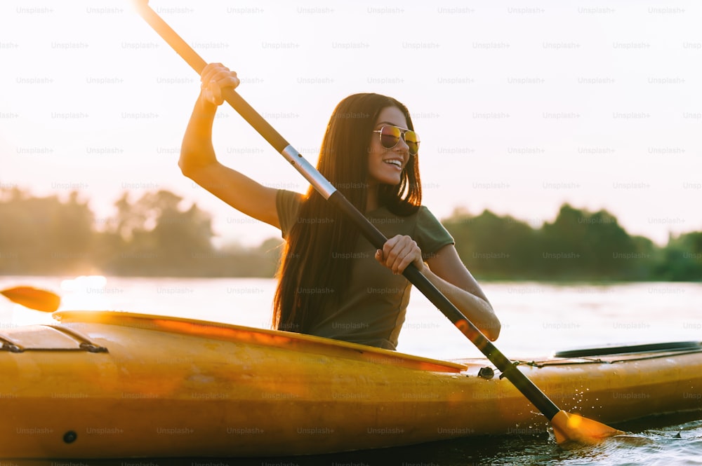 Belle jeune femme souriante pagayant tout en étant assise dans un kayak