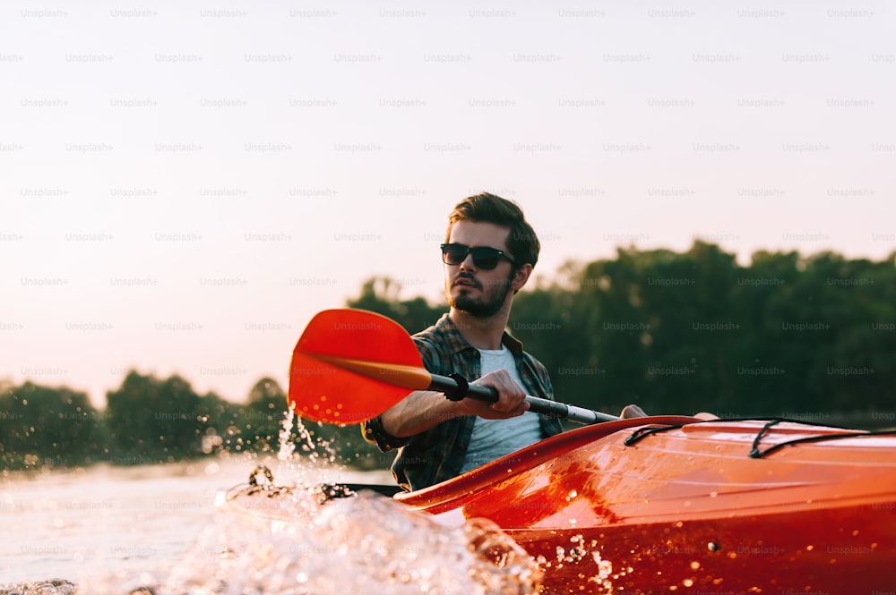 夕日を背景に湖でカヤックを漕ぐ自信に満ちた若い男