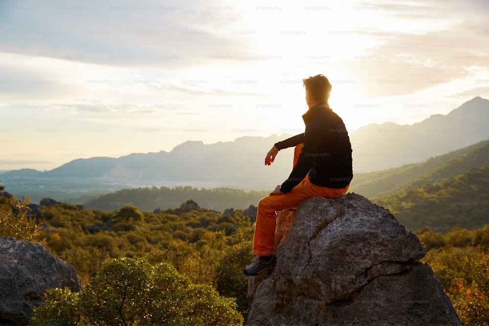 male traveler  standing on the cliff against mountains and cloudy  sky at early morning